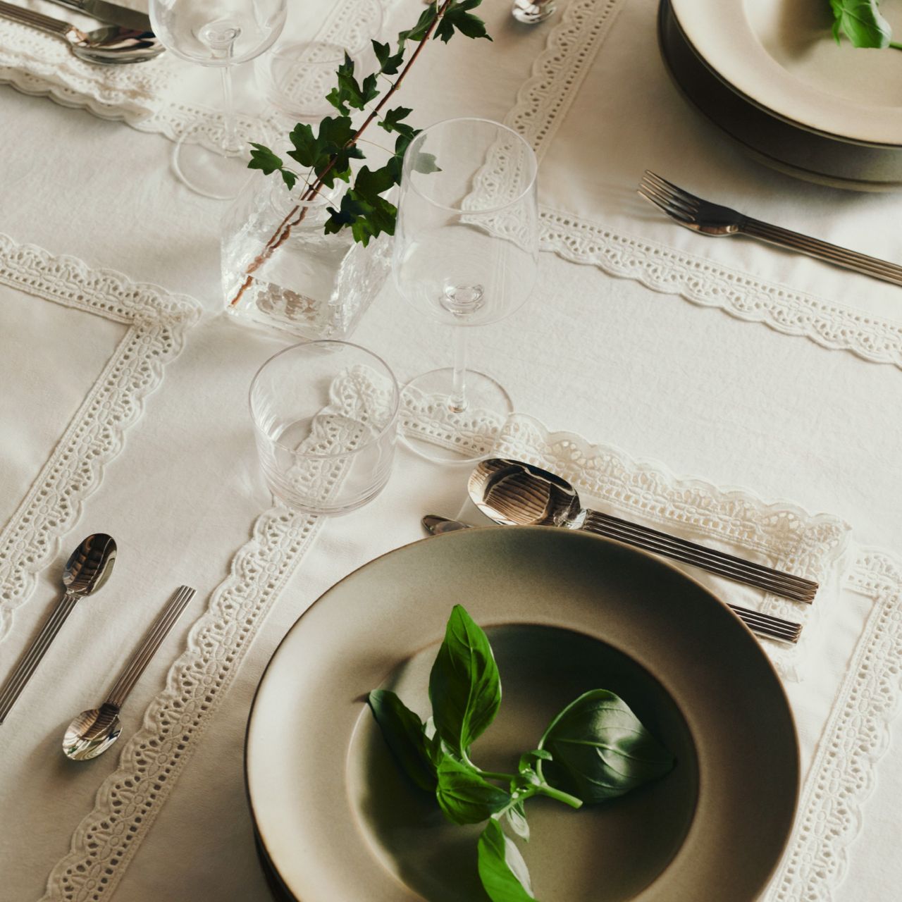 A set dining table with a white tablecloth and white lace-trimmed placemats and napkins from H&amp;M Home's spring/summer 2026 collection 