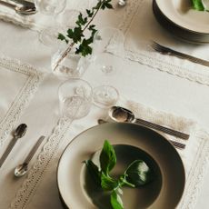 A set dining table with a white tablecloth and white lace-trimmed placemats and napkins from H&M Home's spring/summer 2026 collection 