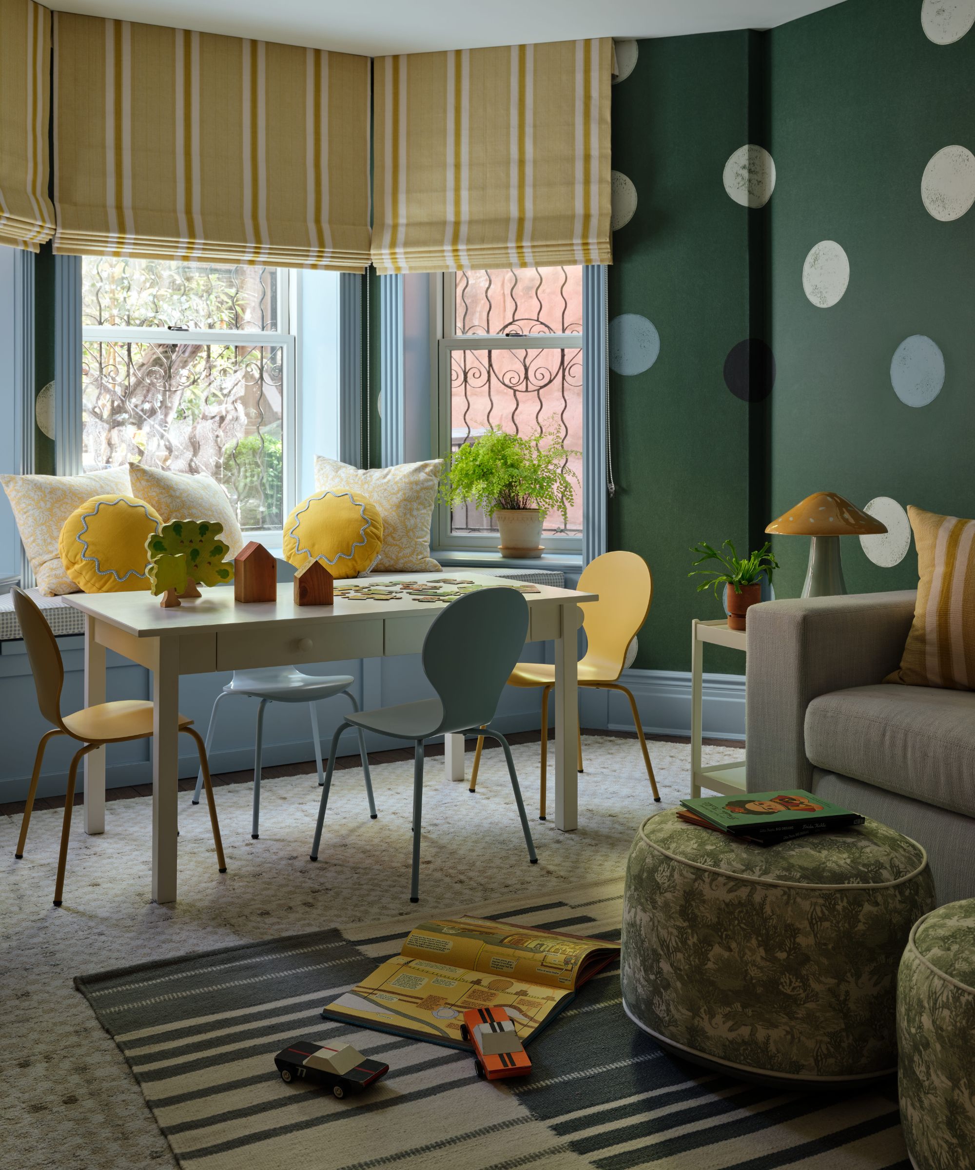 a green polka dot playroom with kids banquette and table and chairs, a couch, little leafy ottomans and a striped rug