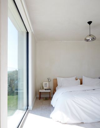 All white bedroom with silver pendant light and picture window
