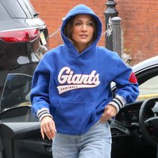 Jennifer Lopez wears a blue giants sweatshirt, light-wash wide-leg jeans, and white sneakers.