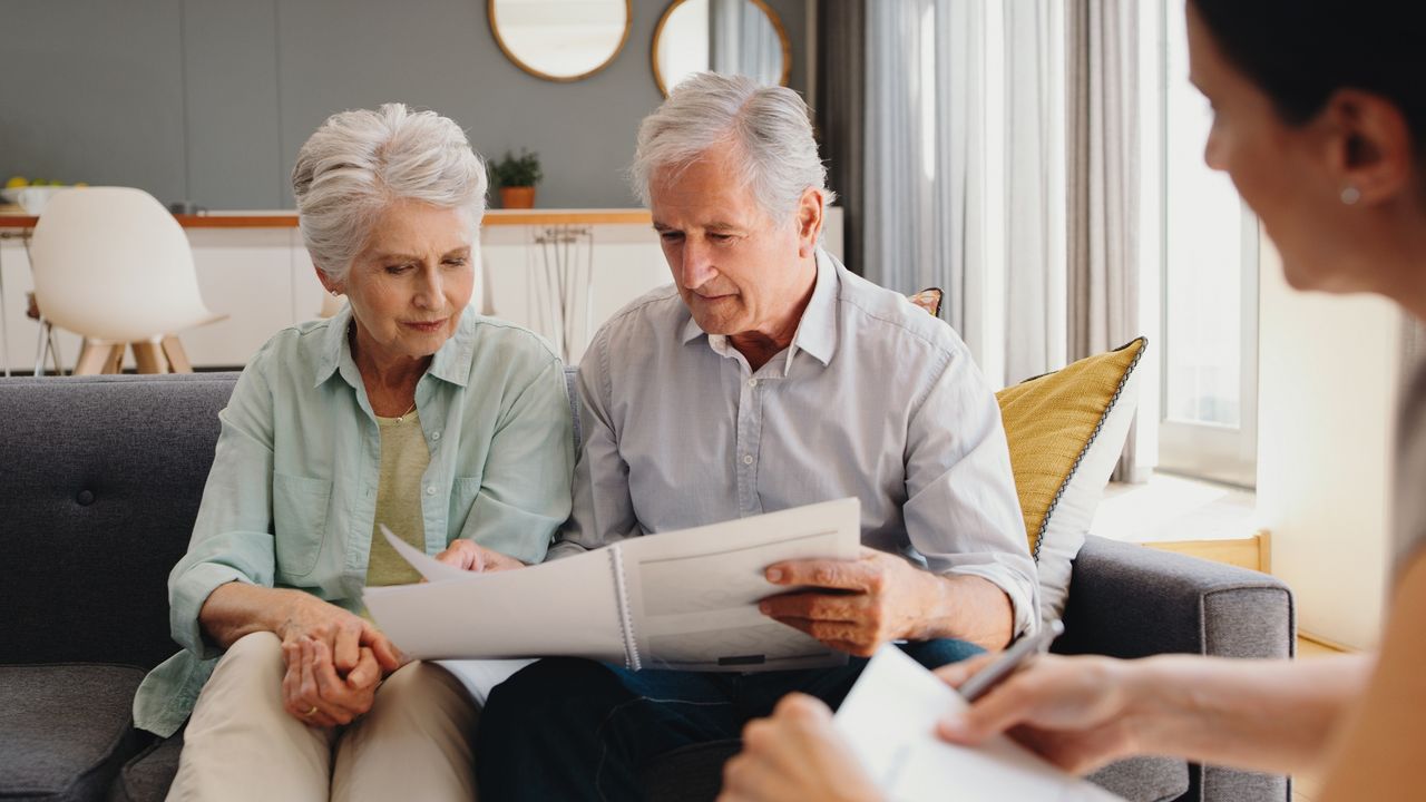 An older couple look at paperwork while sitting on a sofa in a financial planner&#039;s office.