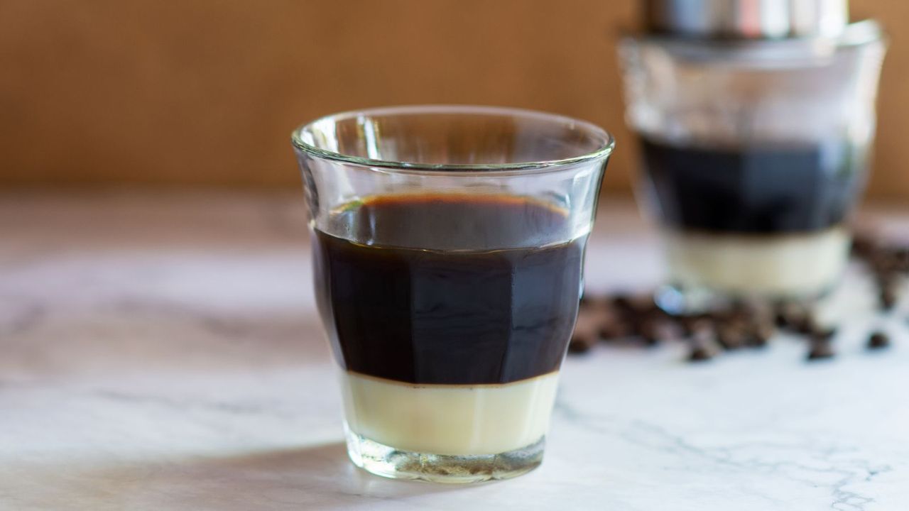 Vietnamese coffee on a countertop with coffee beans and another glass of Vietnamese coffee in the background