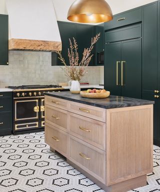 A kitchen with a black and brass range, pale wood island and dark green cabinetry