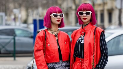 Twins Ami Amiaya & Aya Amiaya wears red cropped jacket, black white skirt, wide leg shorts, sleeveless jacket, black white striped jumper with logo outside Chanel during Paris Fashion Week - Womenswear Fall Winter 2023 2024 : Day Nine on March 07, 2023 in Paris, France.