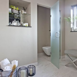 white tiled bathroom with glass door and walled storage