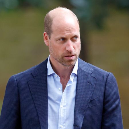 Prince William wears a blue suit with an open shirt and has beard stubble