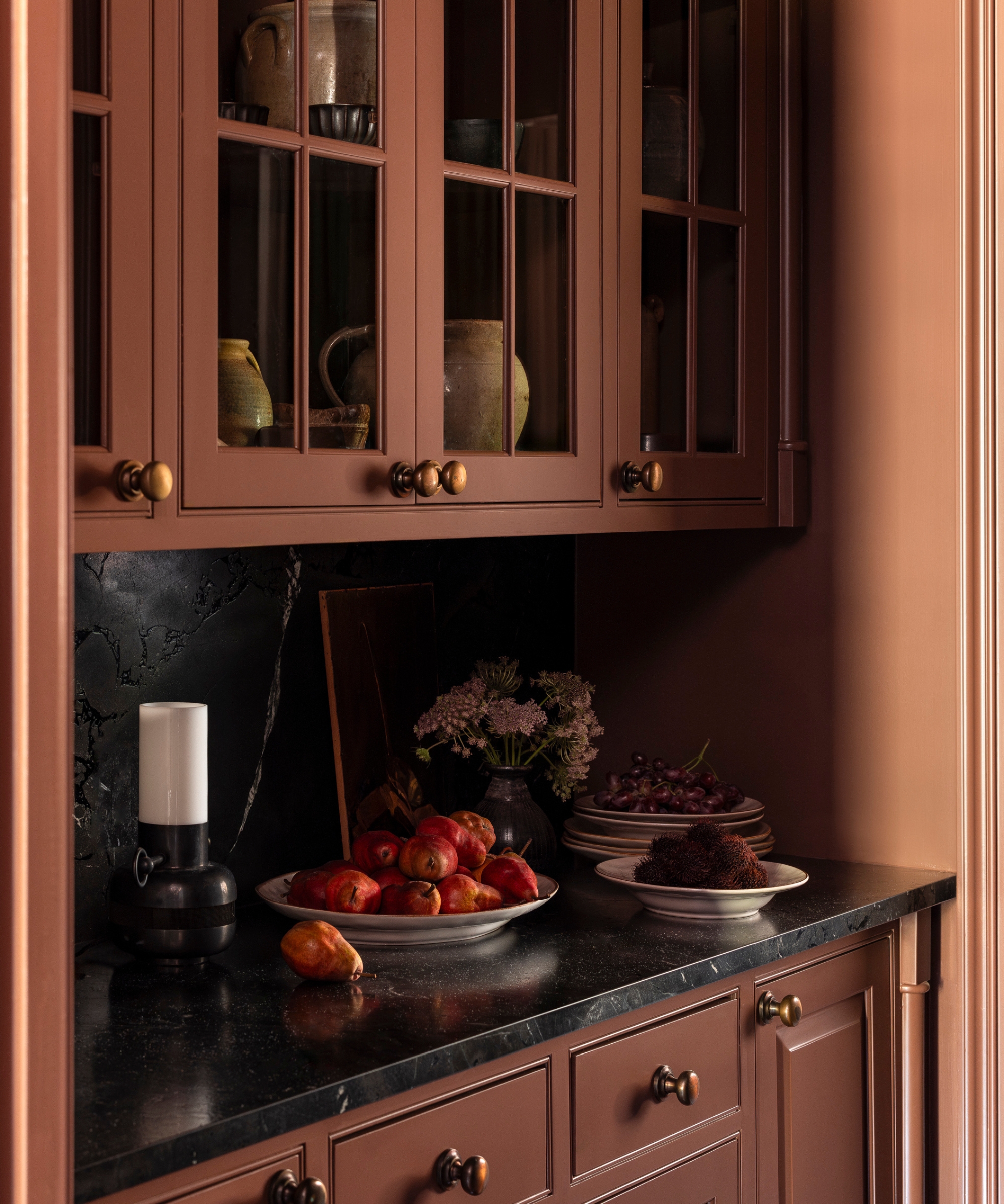A deep red pantry with glazed cabinets and copper hardware
