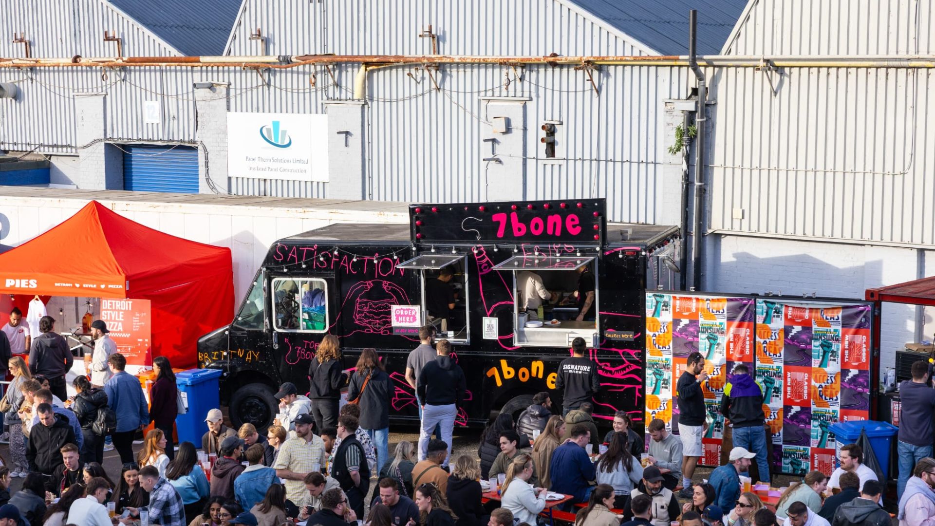 an image of an outdoor food festival with food trucks around the edge of an area and plenty of benches with people eating in the centre