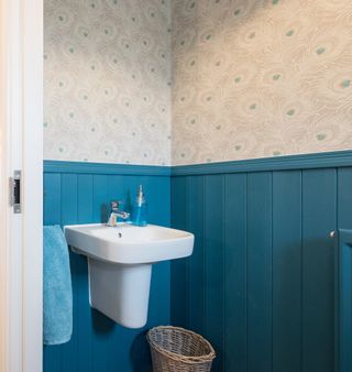 A small bathroom with peacock blue walls and peacock feather wallpaper and nothing on the walls