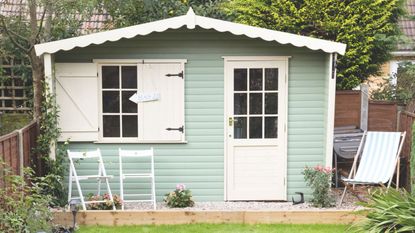 Green garden shed with white accents with three garden chairs in front of it