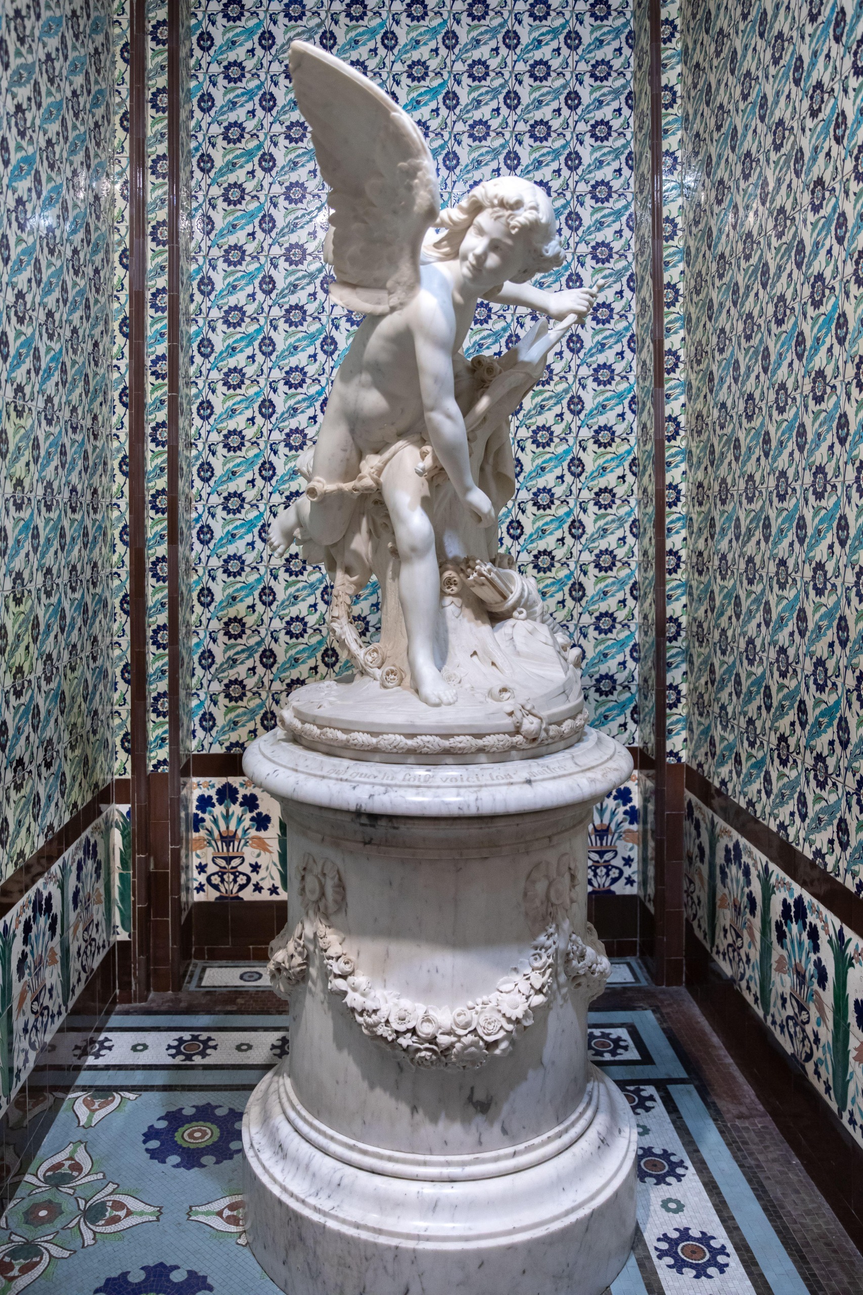 Ottoman tiles and a statue of cupid occupy a room at the Wallace collection. The tiles are blue, the statue is white