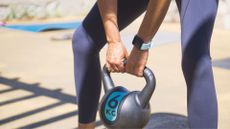 Woman holding a 6kg kettlebell in deadlift position, wearing activewear and a smartwatch as part of the kettlebell workout for beginners