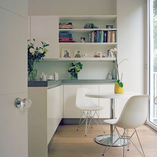 kitchen area with white and grey counter white round table and white chair white shelf and wooden flooring