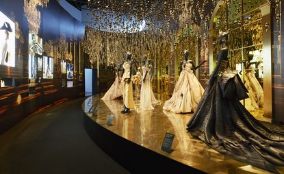 room featuring Dior gowns, above which hangs a ceramic installation of perfume bottles
