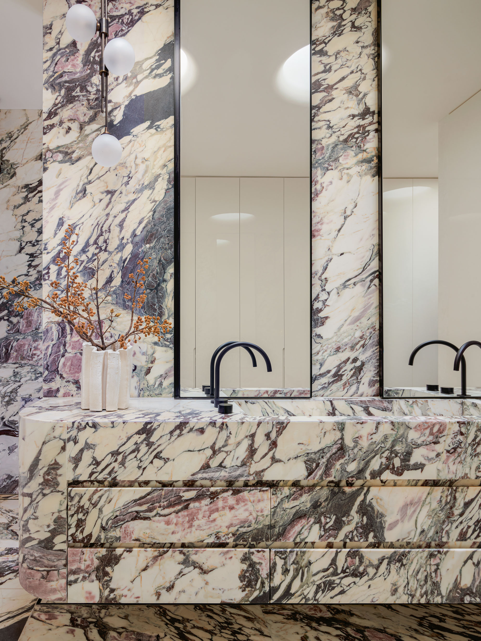 A marble drenched bathroom with subtle shades of pink and black tap-ware and mirrors.