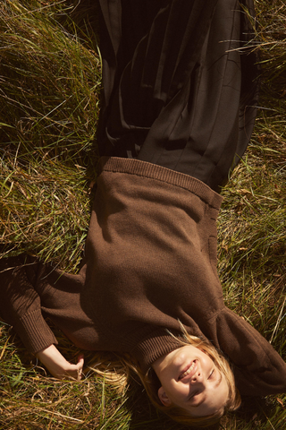 A model wearing a brown sweater by Kotn and laying in the grass