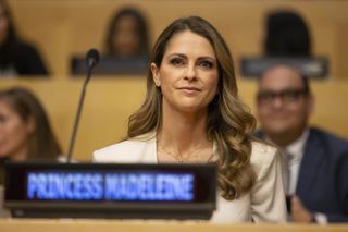 Princess Madeleine wearing a tan suit sitting in front of a mic at the UN