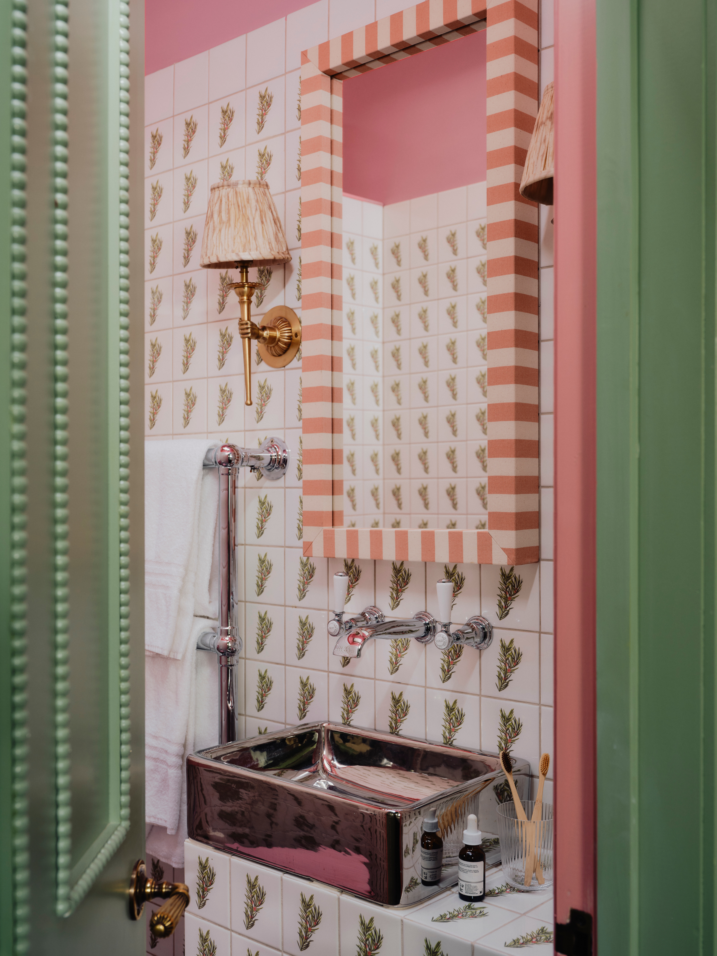 Bathroom with white patterned tiles, pink and white striped mirror, green door and chrome sink