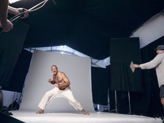 Vincent Cassel in a photography studio on a grey backdrop, wearing white trousers, no top,