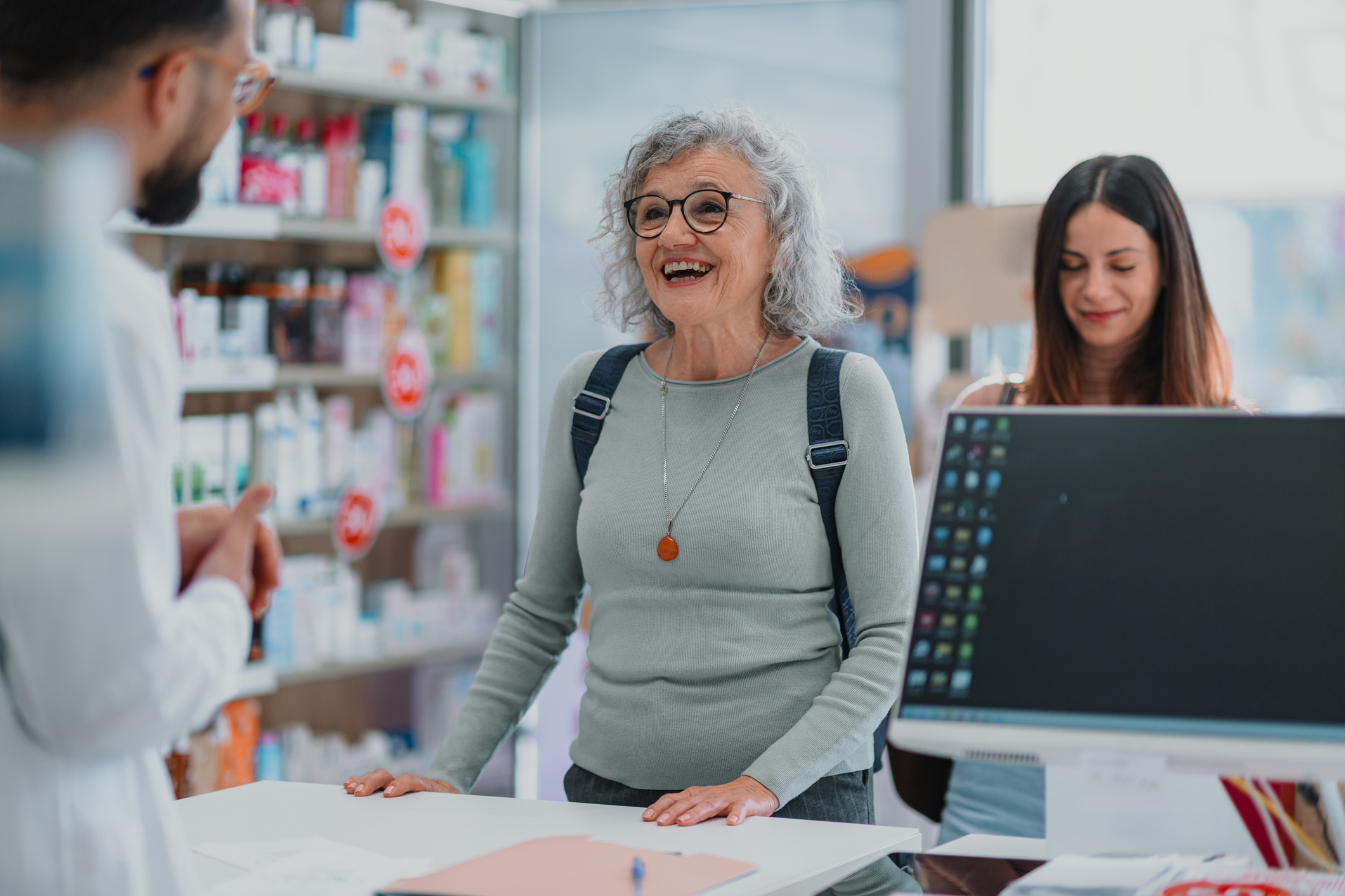 Pharmacist standing at counter, giving medical advice and information to a happy mature adult customer in a drugstore