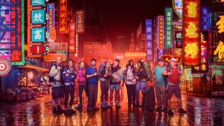 The contestants for Race Across the World season 5 in front of the neon lights of a Chinese city backdrop.