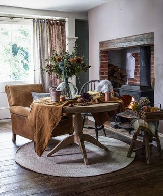 Fall table decor ideas with orange armchair, brick fireplace and orange tablecloth on round table