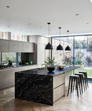 Modern fitted kitchen with grey wood-effect walls and black marble kitchen island on parquet floor