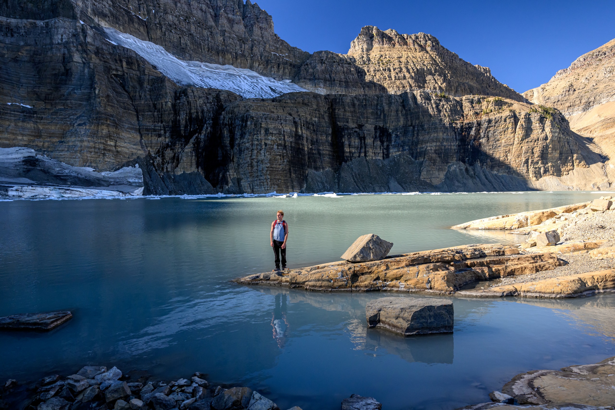 A hiker stands at the edge of Grinnell Lake in Glacier National Park.