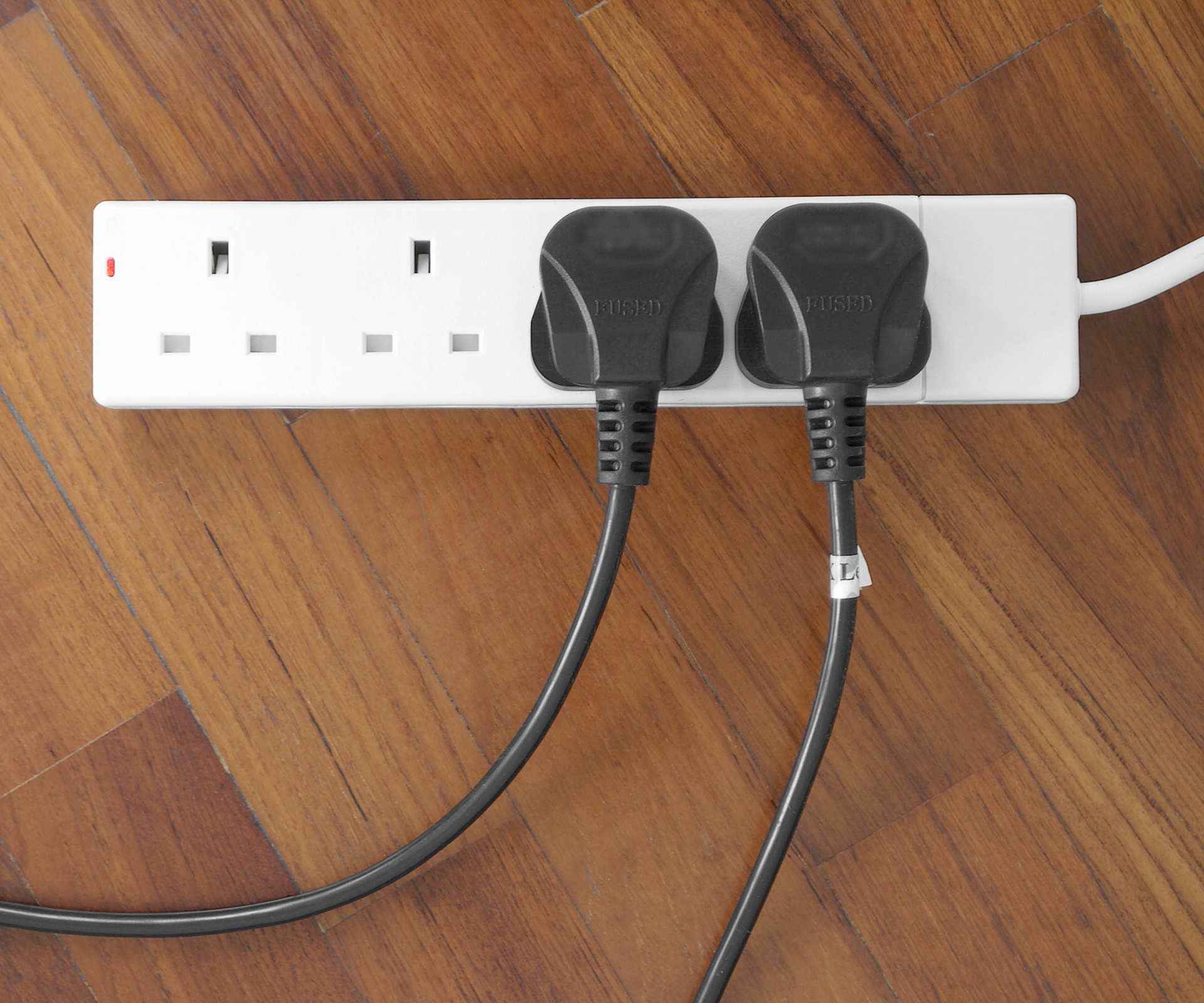 two leads plugged into a white extension lead on wooden floor