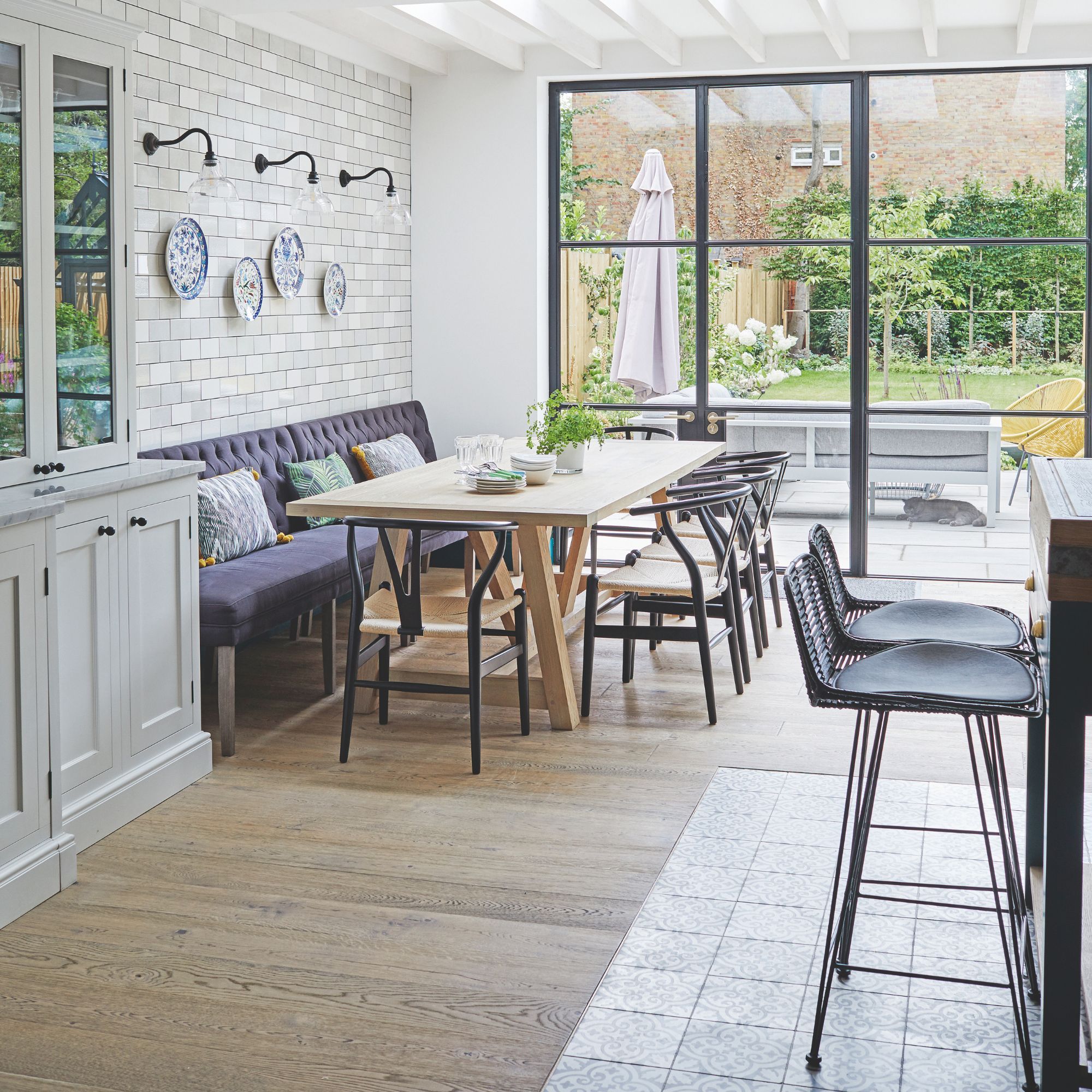 Open plan kitchen-dining area with bench seating and a wooden dining table next to big patio doors leading to a garden