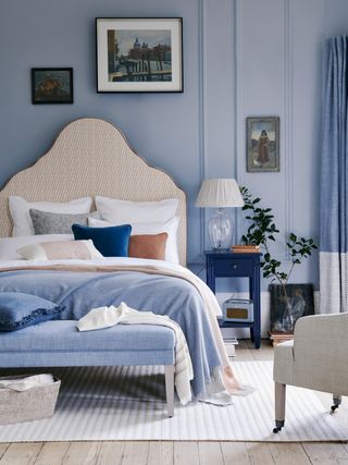 Blue bedroom with tall headboard and a side table with lamp on, illustrating how to make a small bedroom look bigger