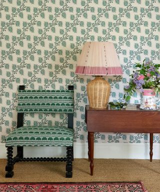 upholstered chair and dark wood table in a hallway papered in green vine wallpaper