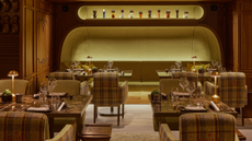 The Maya hotel courchevel restaurant with a space age meets traditional scheme with tartan armchairs at tables with table lamps and a large backlot green banquette seating area at the back with a backlot alcove above with decorative items