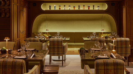 The Maya hotel courchevel restaurant with a space age meets traditional scheme with tartan armchairs at tables with table lamps and a large backlot green banquette seating area at the back with a backlot alcove above with decorative items