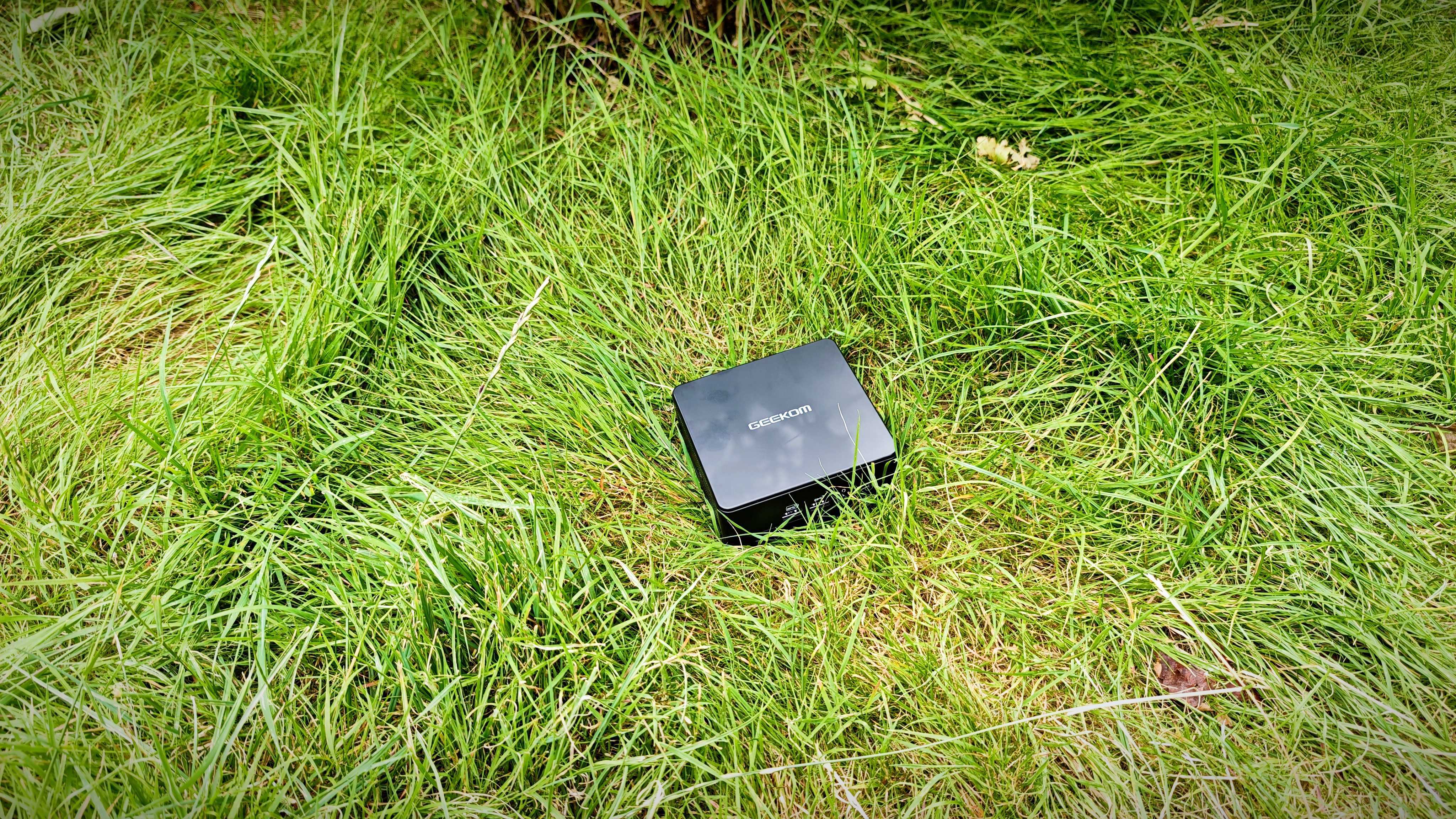 A black Geekom IT15 mini PC sitting in a grassy field