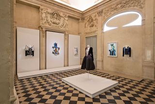 View of the Musée National Picasso-Paris tribute to Yves Saint Laurent featuring wall art and fashion pieces on display in a room with decorative and stone coloured walls and checked flooring