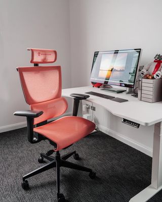 The ErgoTune Supreme V3 office chair in red, sitting behind a desk with a computer.