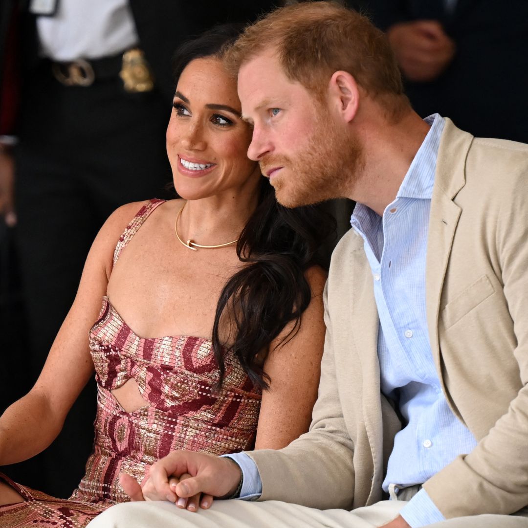 Meghan Markle and Price Harry sit side by side watching a performance while meghan markle wears a colorful dress