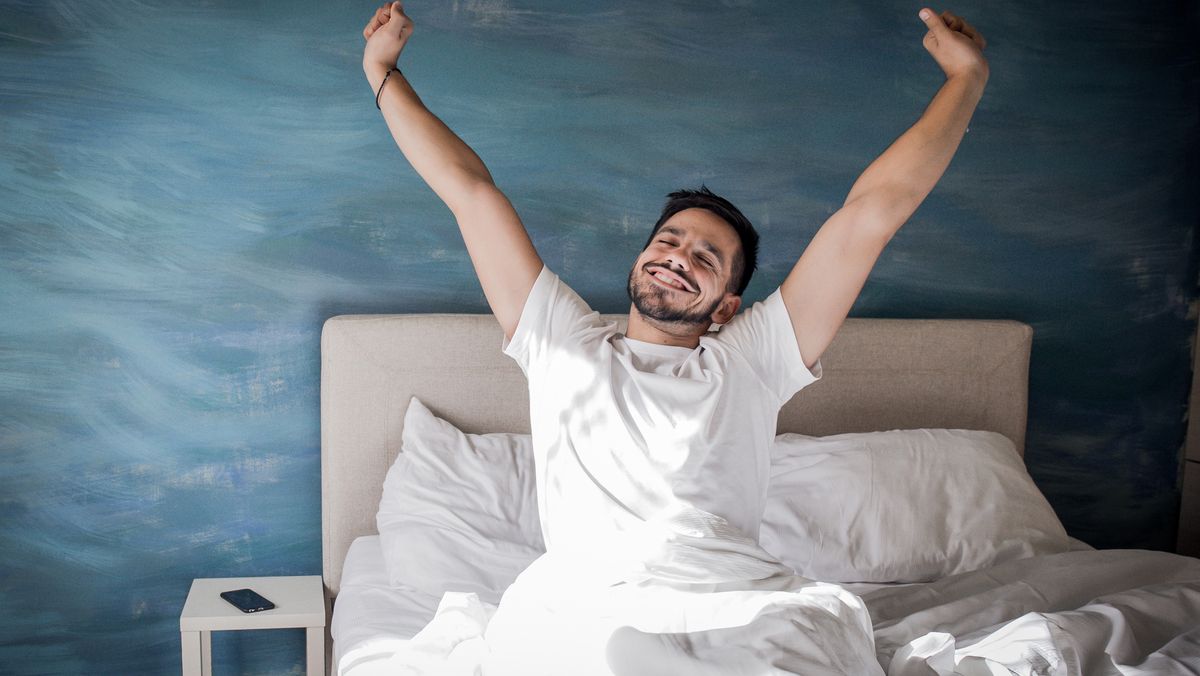 A man wakes up happy and stretches out his back after a great night&#039;s sleep