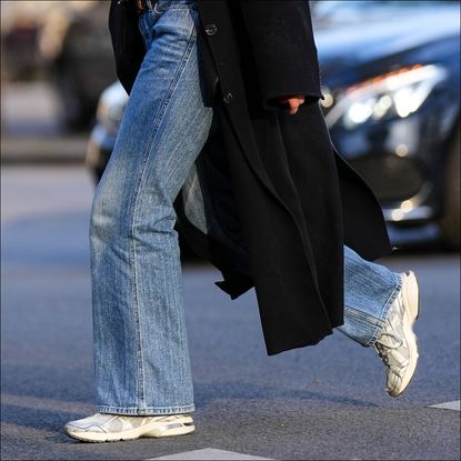 : A passerby wears a red embossed striped pattern zipper high neck cardigan, a black wool long coat, blue faded denim wide legs pants, white and silver shiny leather sneakers from Asics, during a street style fashion photo session, on April 09, 2023 in Paris, France