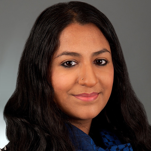 A woman with long dark hair wearing a blue and black shirt smiles for the camera.
