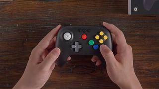 Hands holding modded black 8Bitdo N64 controller with colorful buttons.