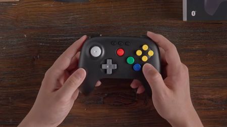 Hands holding modded black 8Bitdo N64 controller with colorful buttons.