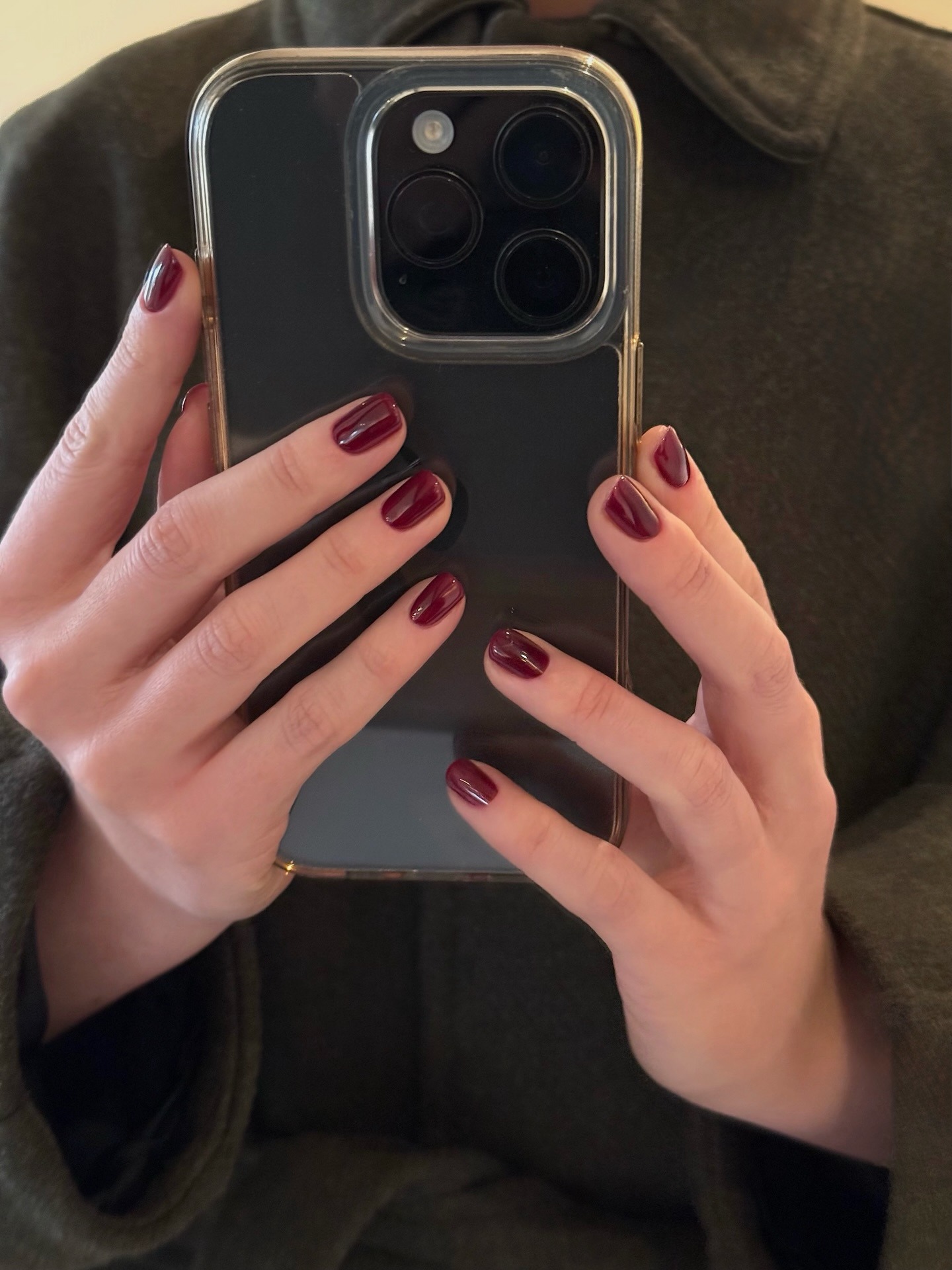 A woman holding an iPhone with a ruby red manicure