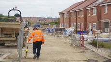 A worker in high-vis jacket and a digger on a new-build housing estate under construction