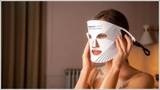 woman wearing CurrentBody LED Light Therapy mask and holding it up on her face