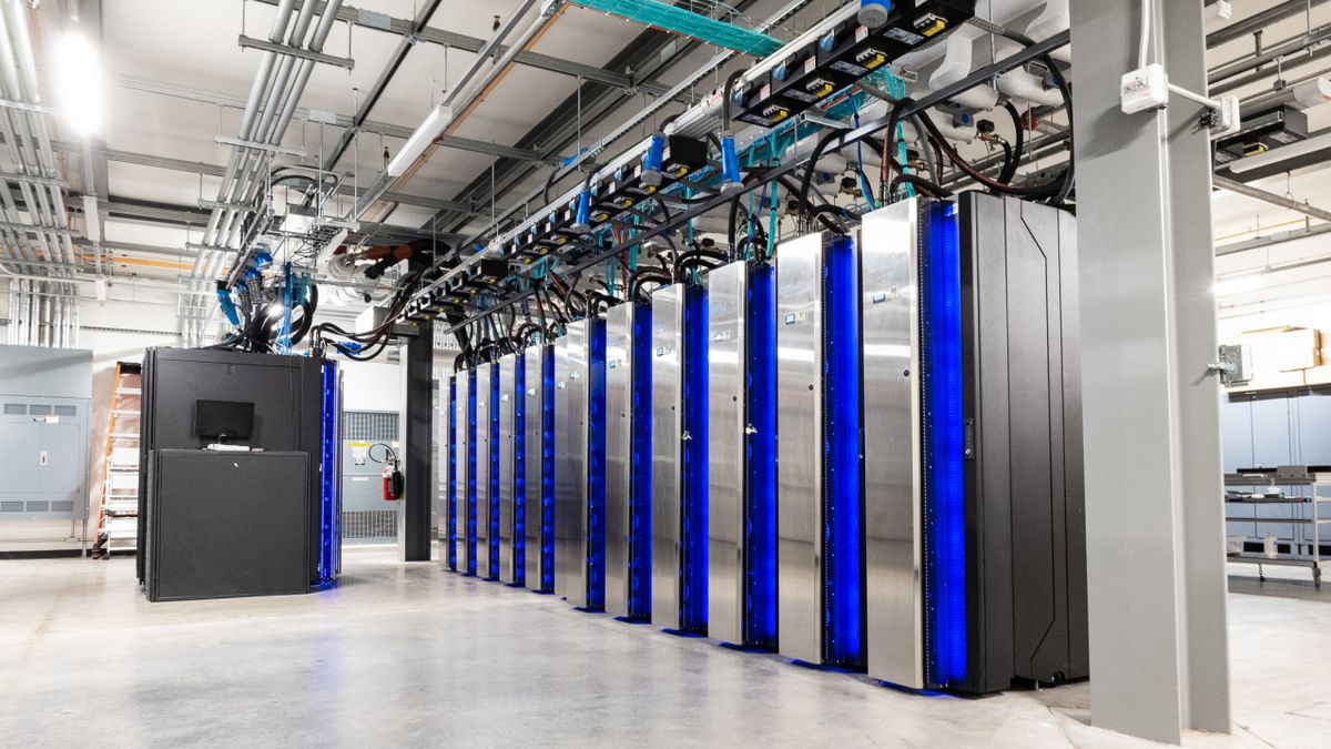 A bank of boxes make up a supercomputer in a clean, brushed metal room, with blue light emanating from each box