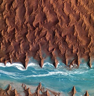 Namib Desert, southwest Africa: Sand dunes, some reaching higher than 300 meters (about 1,000 feet), dominate the world's oldest desert. The blue-and-white area is the dry riverbed of the Tsauchab, which only sees water following rare rainfall in the Naukluft Mountains to the east.