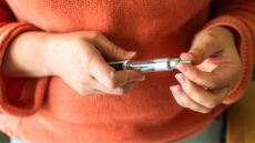 Woman holding Mounjaro medication in hands, taking the lid off, wearing bright jumper at home, after wondering what happens when you come off Mounjaro